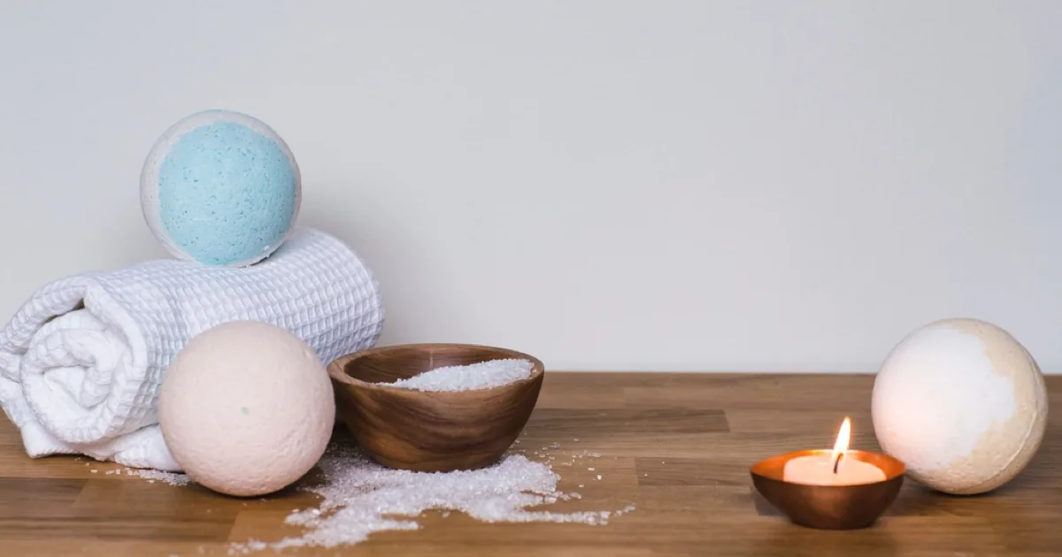 Serviette blanche roulée, boules effervescentes, bol de sel de bain et bougie allumée