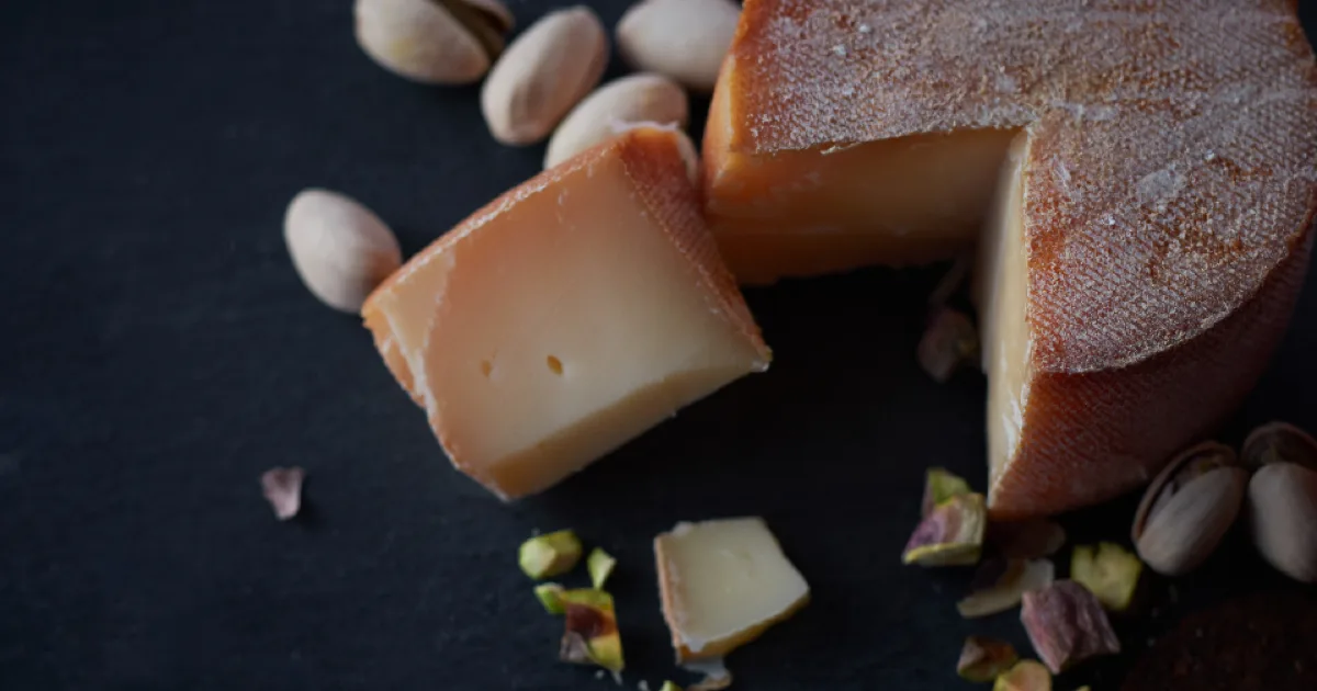 Meule de fromage entamée entourée de pistaches sur une ardoise sombre