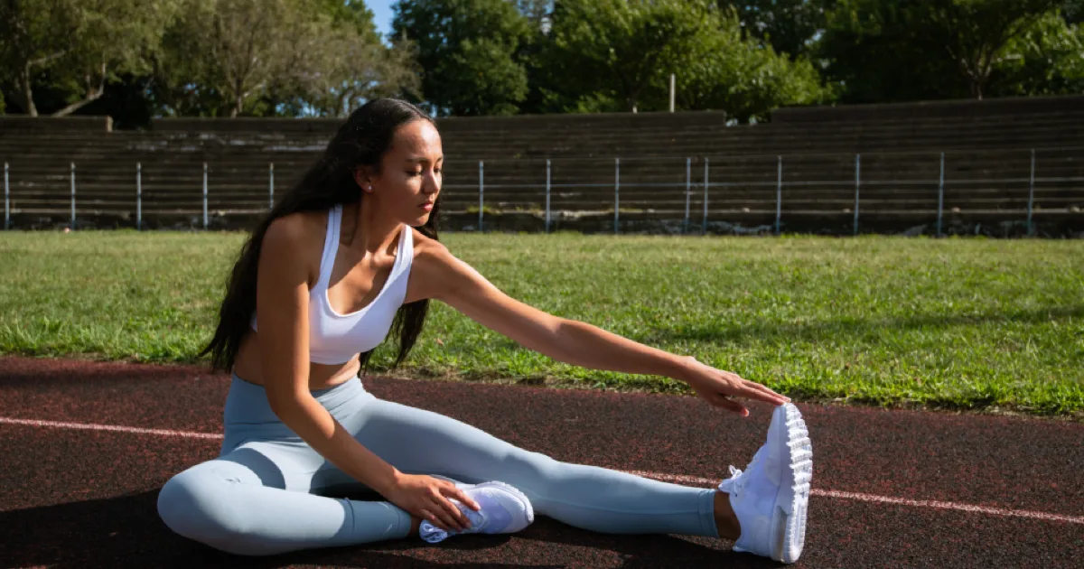 Sportive assise sur une piste d'athlétisme réalisant un étirement des ischio-jambiers