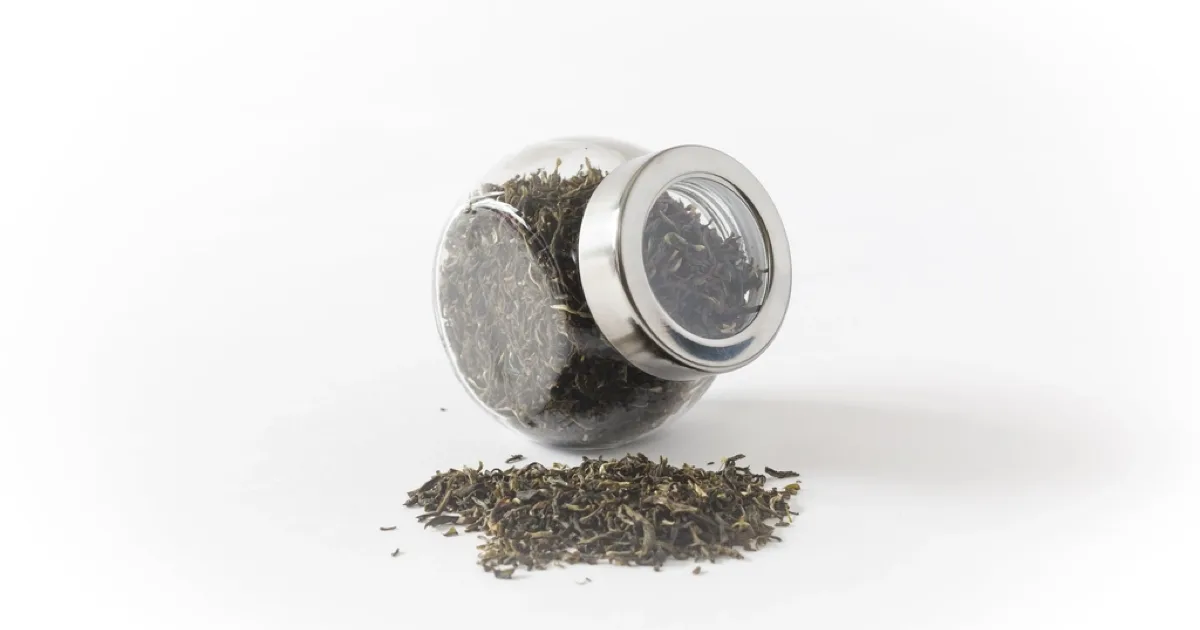 Bocal en verre de thé noir en feuilles, un peu de thé répandu à côté