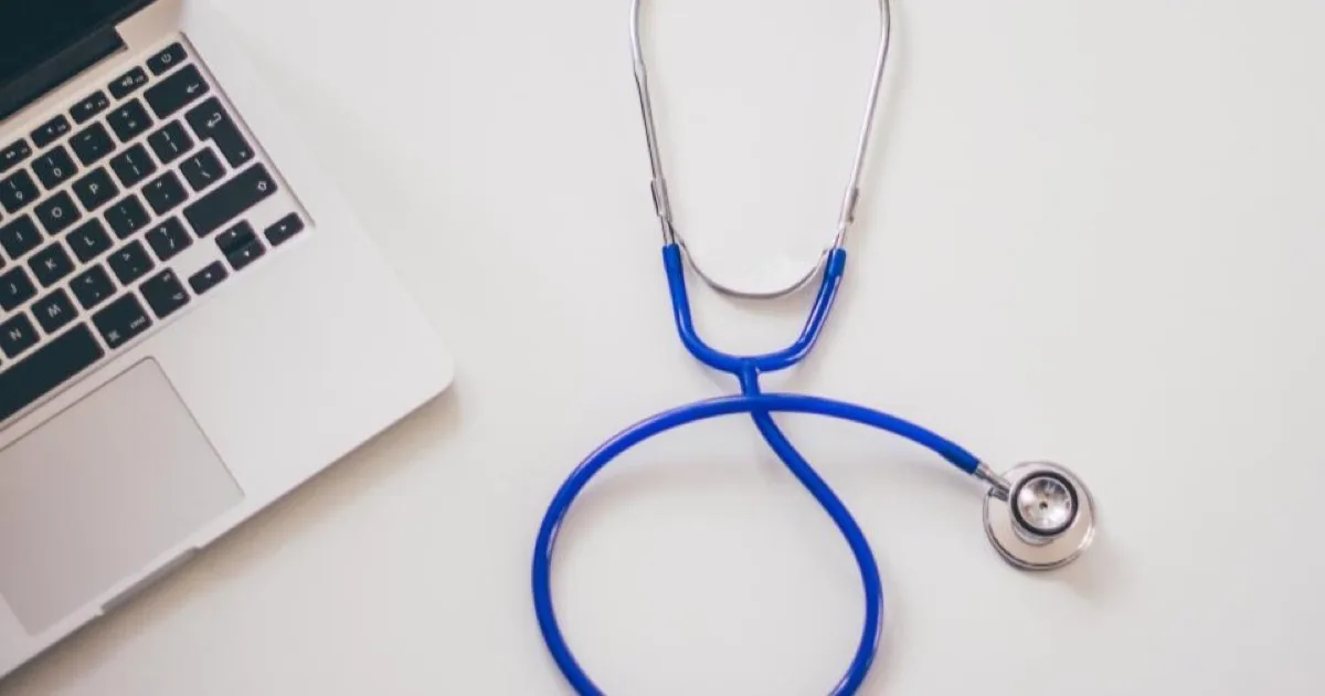 Stéthoscope bleu posé à côté d'un ordinateur portable sur un bureau, illustrant la gestion administrative en santé