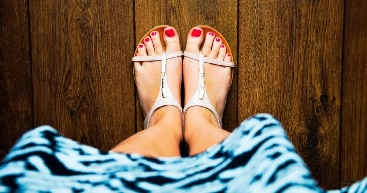 Pieds en sandales vus de dessus sur un parquet en bois