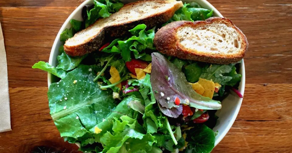 Bol de salade verte avec tranches de pain grillé sur une table en bois