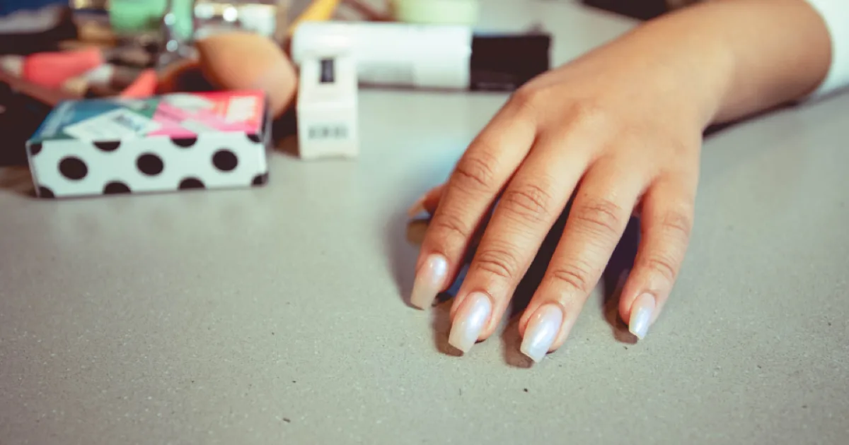 Main aux ongles longs manucurés posée sur une table, produits de manucure en arrière-plan