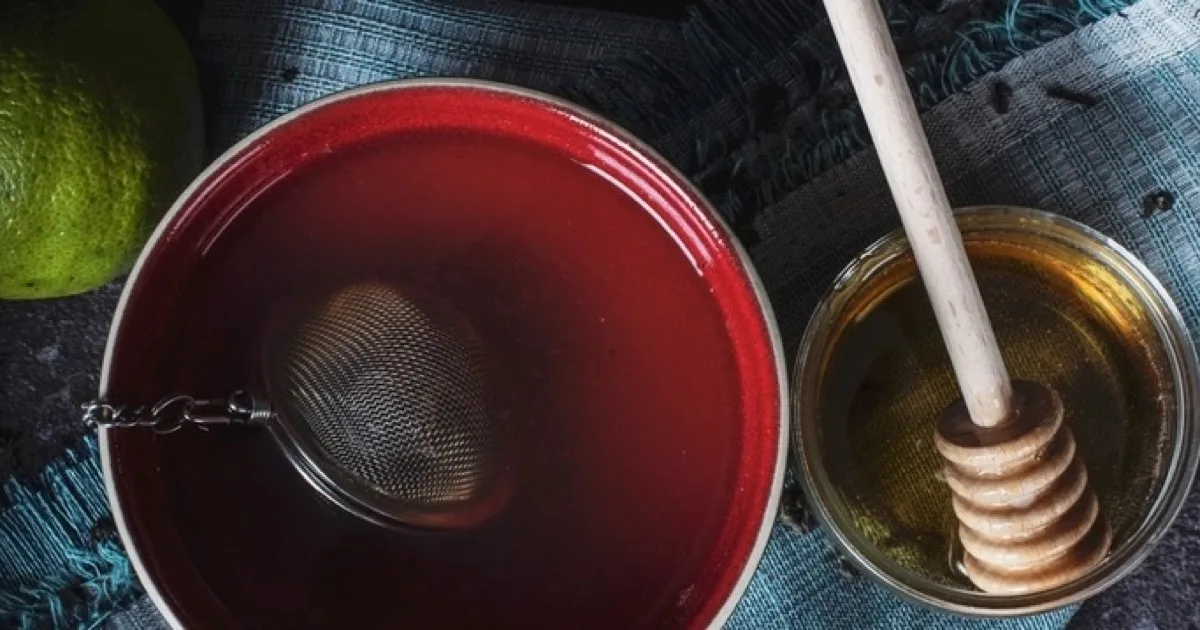 Tisane infusée dans un bol rouge, avec du miel et des citrons verts coupés