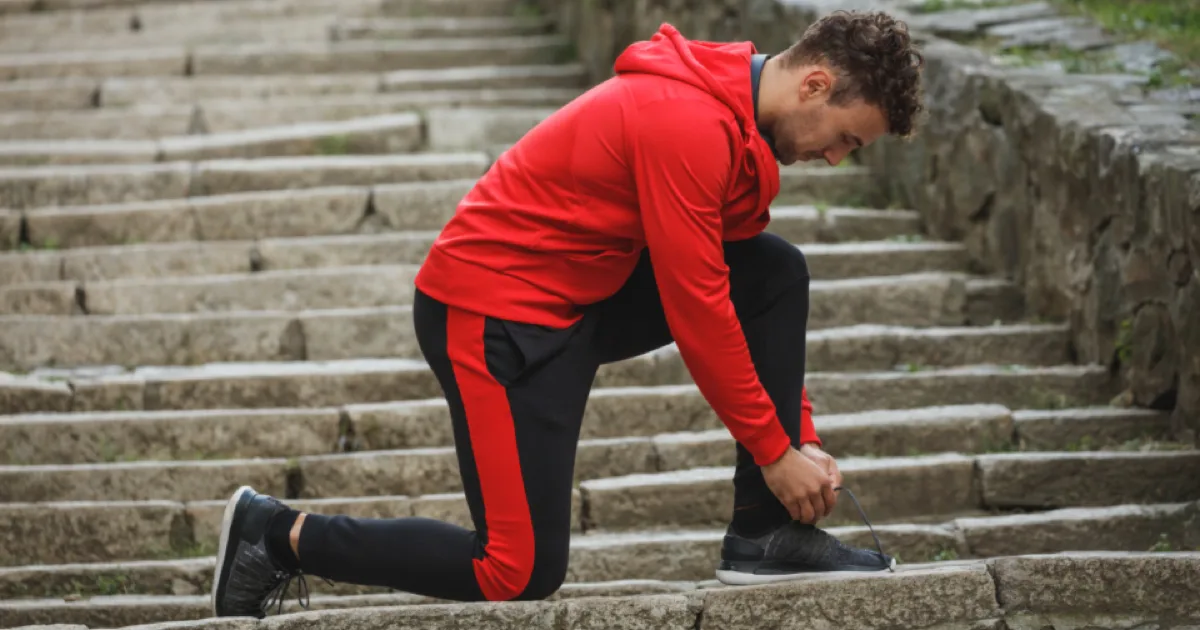 Homme agenouillé sur des marches en pierre, laçant sa chaussure de sport