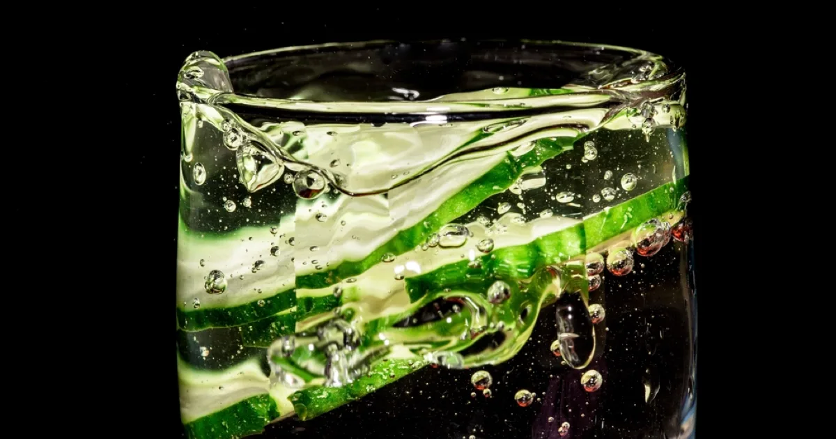 Rondelles de concombre et fines bulles dans un verre d'eau sur fond sombre